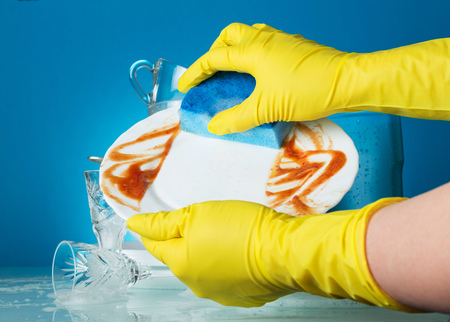 Female hands in yellow gloves wash a dirty plate on a blue backgroundの写真素材