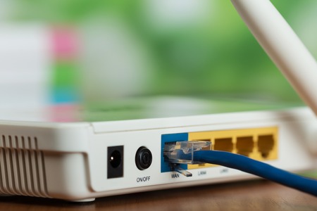 The connectors of the white router and the blue cable in the bright office. Macroの写真素材
