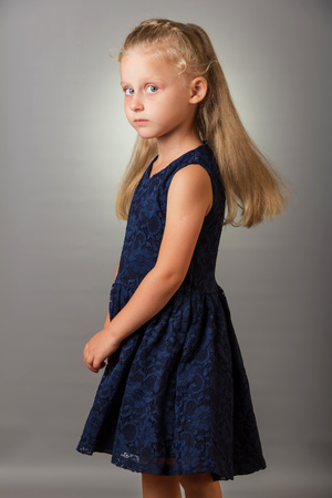 Beautiful blond little girl in a dark blue dress on a gray backgroundの写真素材