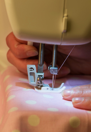 Macro. Female hands on white electric sewing machine pink fabric with pink polka dotsの写真素材