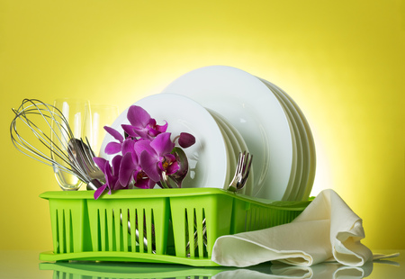 Washed dishes and utensils in the green dryer on a yellow background, an orchid branch and dishwashingの写真素材