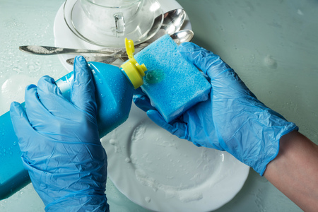 Hands in blue gloves wash the dishes. Sponge for washing and a means of fatの写真素材