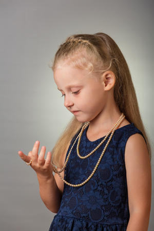 Beautiful blond little girl in a elegant dress on a gray backgroundの写真素材