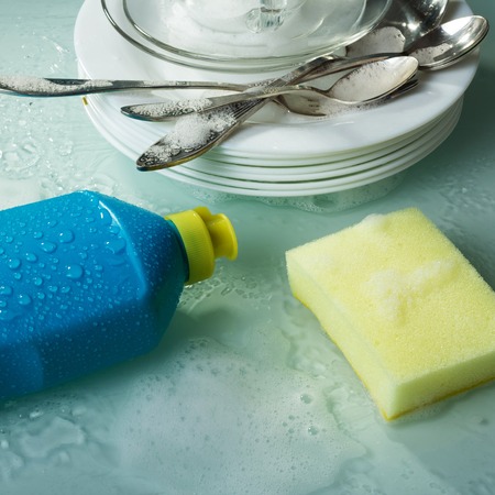 Washing dishes with a special tool, yellow sponge and plates in the foamの写真素材