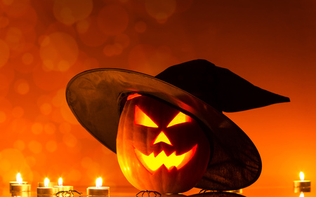 Pumpkin with glowing eyes and candle on bright orange backgroundの写真素材