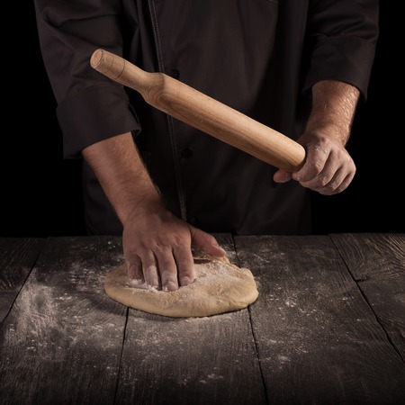 Chef man in a dark jacket roll out the dough isolated on black backgroundの写真素材
