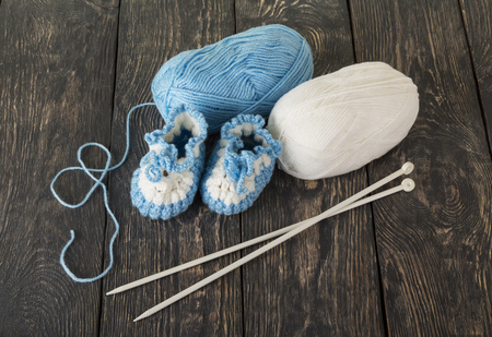 Knitted booties for baby, white and blue skein of wool yarn in dark boardsの写真素材