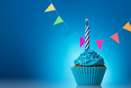 Festive cupcakes for a birthday on a blue background with colorful garland and a candleの写真素材