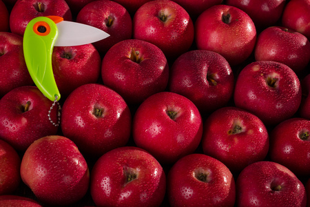 Bright ceramic knife on the background of fresh juicy apples in drops of waterの写真素材