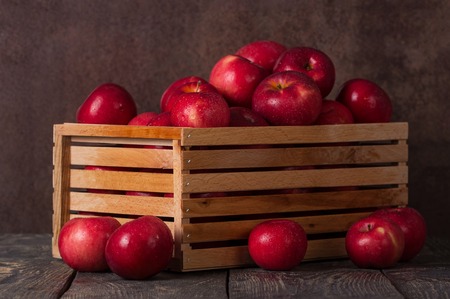 Wooden box full of apples in drops of water on dark boardsの写真素材