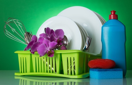 Clean dishes and cutlery in the dryer on a green background decorated with a branch of orchidsの写真素材