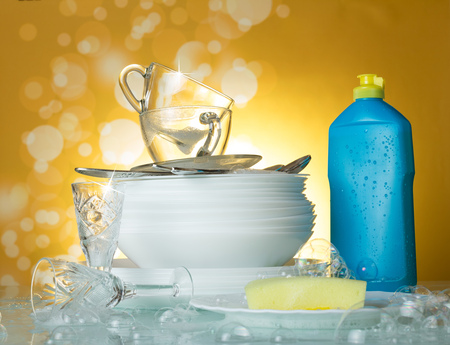 Clean dishes and cups, dishwashing detergent and sponge on a yellow background in soap bubblesの写真素材