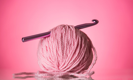 Bright pink ball of wool and a crochet hook on a pink backgroundの写真素材