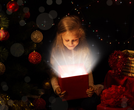 The magic of Christmas. A little girl opens a magical gift on the Christmas treeの写真素材