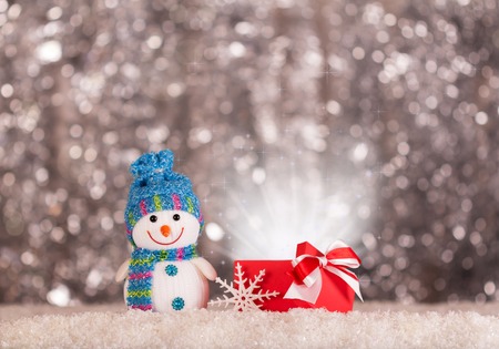 Smiling snowman and a magical gift in the snow on a bright grey backgroundの写真素材