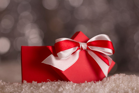 Red Christmas box with bow in the snow on a gray background with bokeh effectの写真素材