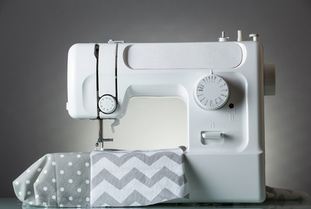 White modern electric sewing machine on a gray background and fabric cutsの写真素材