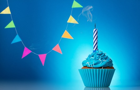 Chocolate cupcake with icing and birthday candle on blue backgroundの写真素材