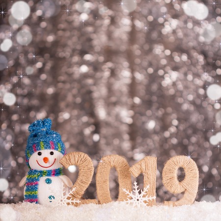 Happy smiling snowman and new year inscription 2019 on bright background with bokeh effectの写真素材