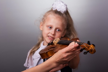 Beautiful little girl playing the violin on bright gray backgroundの写真素材