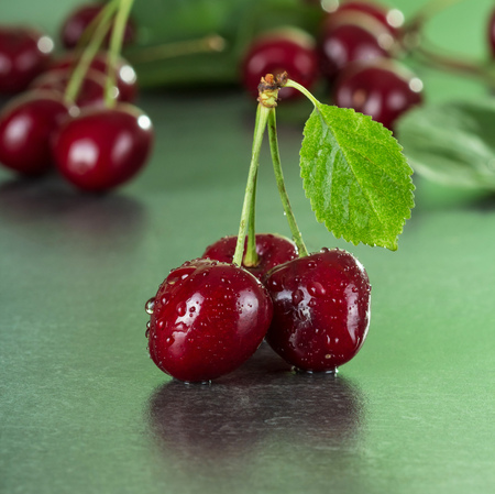Fresh juicy berries cherries with green leaves in water drops on dark tableの写真素材