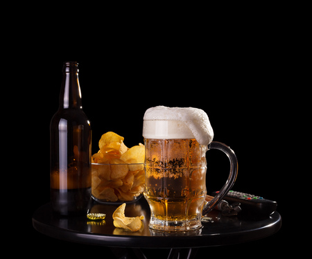 Beer with foam in the glass, crisp chips, watching TV isolated on blackの写真素材