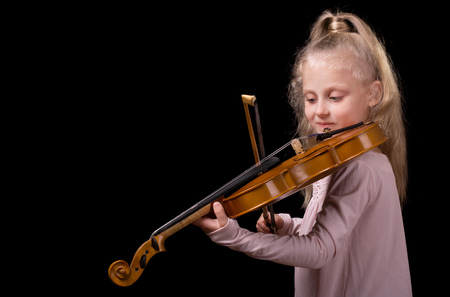 Beautiful little blond girl playing the violin isolated on a black backgroundの写真素材