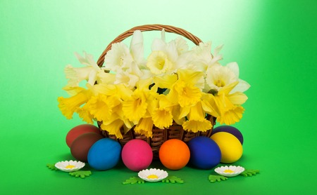 Bouquet of white and yellow narcissuses in a wattled basket, eggs and sweet marzipan flowers, on a green backgroundの写真素材
