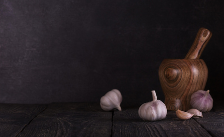 Composition in low key from the mortar for grinding spices and fresh heads of garlic on dark boardsの写真素材