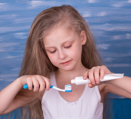 Nice little girl takes care of his teeth, squeezing toothpaste on a toothbrushの写真素材
