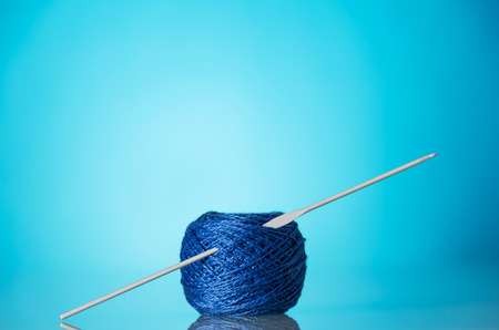 Skein of blue wool yarn for knitting and knitting needles on a bright blue background