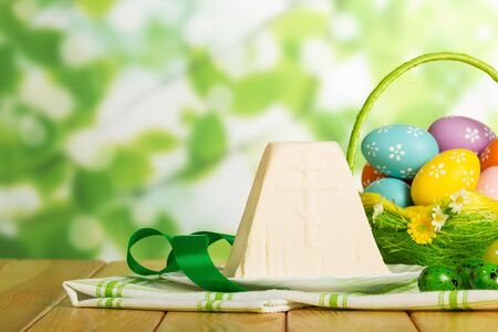 Traditional Easter cheese dessert, colored Easter eggs in basket and near the ribbon on abstract green background.の写真素材