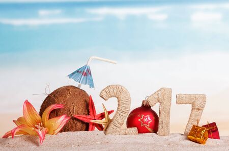 217 Digits twined with twine, Christmas ball instead of the digits 0, coconut, sea stars, gifts and flower in the sand against the sea.の写真素材