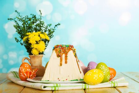 Traditional Easter curds dessert watered glaze and sprinkle with colored Easter eggs, vase with flowers and butterflies on the abstract blue background.の写真素材
