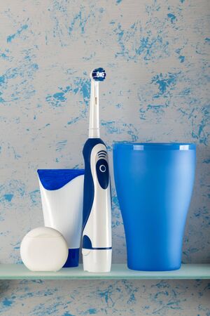 Electric toothbrush, toothpaste and dental floss on glass shelfの写真素材