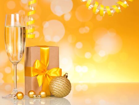 Glass of wine, box with gift, big and small Christmas balls, on yellow sparkling backgroundの写真素材