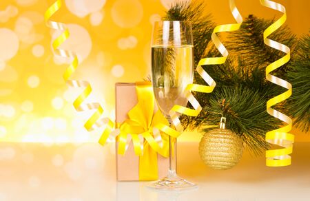 Christmas pine branche are festively decorated, glass of champagne and box with gift, on shimmering yellow backgroundの写真素材