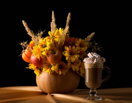 Original composition in the pumpkin, nearby cup of cappuccino with marshmallows, isolated on black backgroundの写真素材