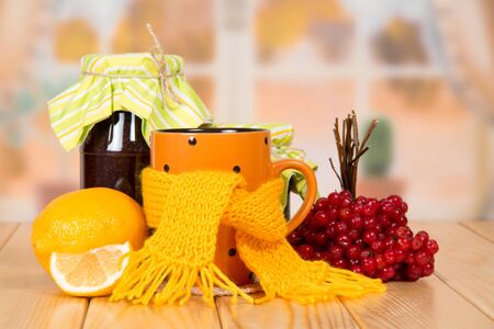 Warming tea from a viburnum, jars with jam and lemon, on a wooden tableの写真素材