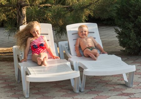 Little boy and girl with luxurious hair sitting in lounge chair, on nature backgroundの写真素材