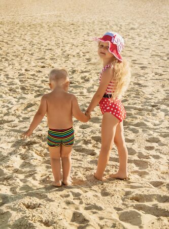 Little girl and boy are walking along the sandy beach, holding handsの写真素材