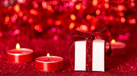 Romantic valentine's day. Candles and gift box on a sparkling red backgroundの写真素材