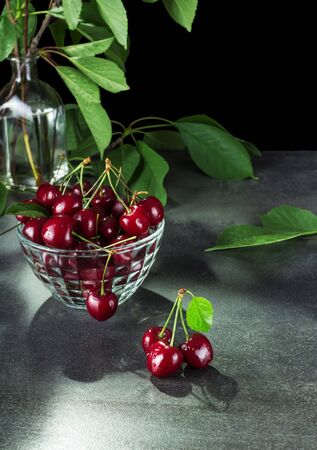 Ripe red cherries with tails in glass bowl, on grey surfaceの写真素材