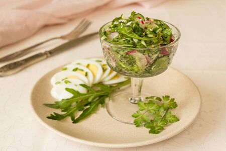 Salad of arugula and radish with sesame and egg in glass salad bowl, on beige tableclothの写真素材