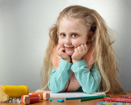 Little girl sits at table with warm scarf around her neck, near inhaler and medicineの写真素材