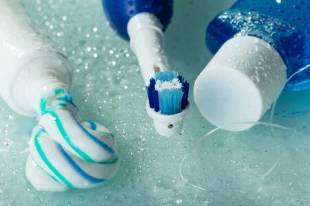 Electric toothbrush, paste and mouthwash, on wet glass shelf. Closeup