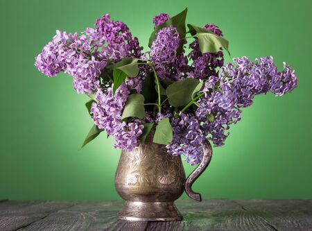 Bouquet of fragrant lilac in vintage vase, on green backgroundの写真素材