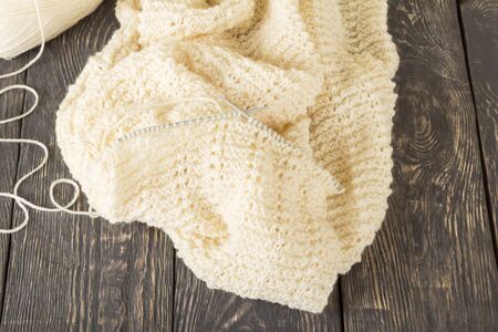 Knitted product of light soft yarn handmade, and knitting needles, on wooden tableの写真素材