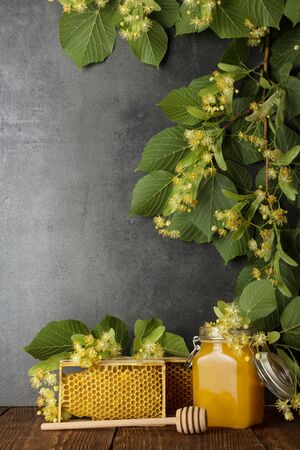 Jar with honey, honeycomb and stirrer on gray background, on top of branch of flowering Lindenの写真素材