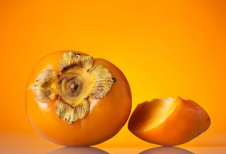 Whole fruit of persimmon and cut piece, on bright orange backgroundの写真素材